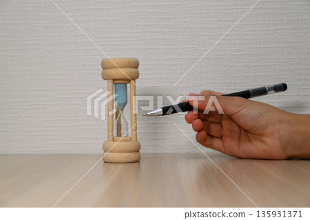 Hand pointing at hourglass with pen and copy space Hand pointing at hourglass with pen and copy space 135931371