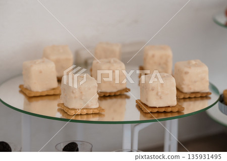 Elegant White-Covered Dessert Cubes on Gingersnap Biscuits Arranged on Glass Tiered Stand 135931495