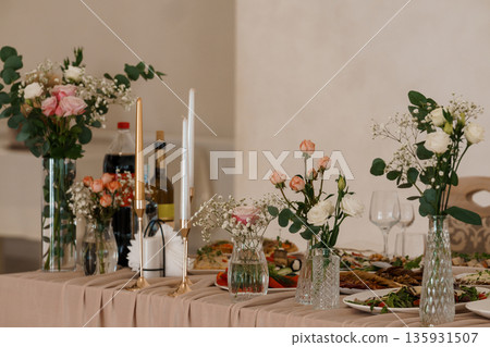 Elegant Table Setting with Rose Bouquets, Candles, and Gourmet Food Arrangement in Soft Pastel Tones 135931507