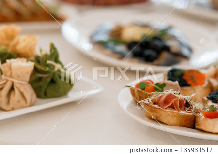 Elegant Appetizer Platter with Crostini, Prosciutto, Olives, and Fresh Herbs on White Tablecloth Elegant Appetizer Platter with Crostini, Prosciutto, Olives, and Fresh Herbs on White Tablecloth 135931512