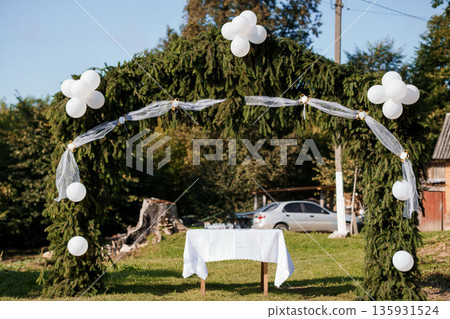 Rustic Outdoor Wedding Arch Decorated with Pine Branches and White Balloons Under Sunny Sky Rustic Outdoor Wedding Arch Decorated with Pine Branches and White Balloons Under Sunny Sky 135931524