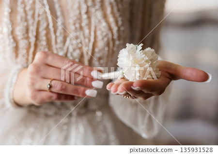 Elegant Bride Holding White Carnation Boutonniere in Beaded Wedding Dress, Close-Up Portrait with Soft Focus Background 135931528