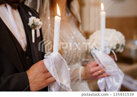 Romantic Wedding Couple Holding Lit Candles in Elegant Church Ceremony with Soft Warm Lighting and White Lace Details 135931539
