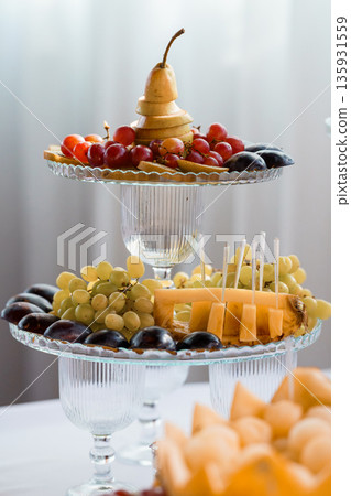 Elegant Two-Tier Glass Fruit Platter with Grapes, Pears, and Cheese for Party Buffet and Catering Events Elegant Two-Tier Glass Fruit Platter with Grapes, Pears, and Cheese for Party Buffet and Catering Events 135931559