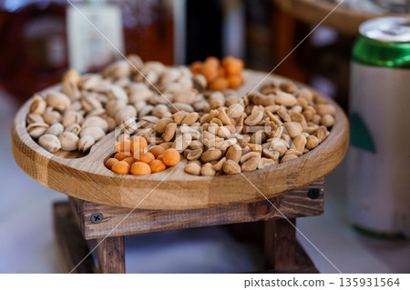 Wooden Nut Platter with Pistachios, Peanuts, and Orange Snacks on Rustic Table with Beverage Can in Background Wooden Nut Platter with Pistachios, Peanuts, and Orange Snacks on Rustic Table with Beverage Can in Background 135931564