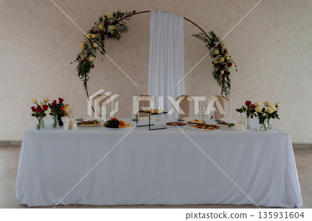 Elegant Wedding Reception Table with Floral Arch Decor and White Linen Arrangement in Soft Natural Light Elegant Wedding Reception Table with Floral Arch Decor and White Linen Arrangement in Soft Natural Light 135931604