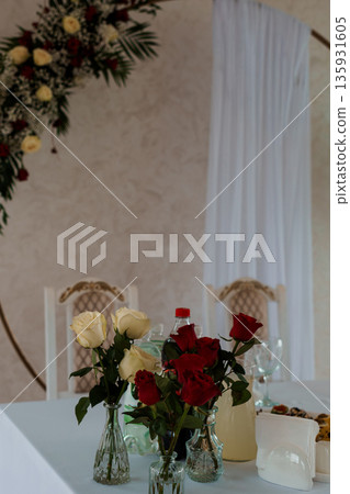 Elegant Wedding Table Setting with Red and White Roses in Glass Vases Under Floral Arch Decoration Elegant Wedding Table Setting with Red and White Roses in Glass Vases Under Floral Arch Decoration 135931605