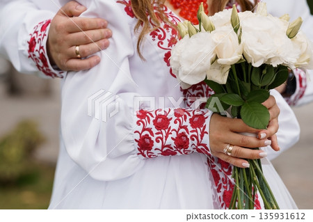 Traditional Ukrainian Wedding Couple Embracing in Embroidered Bridesmaid Dress with White Rose Bouquet Traditional Ukrainian Wedding Couple Embracing in Embroidered Bridesmaid Dress with White Rose Bouquet 135931612