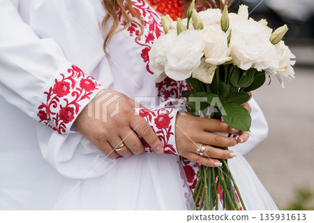 Traditional Ukrainian Wedding Dress with Red Embroidery and White Rose Bouquet Held by Bride Traditional Ukrainian Wedding Dress with Red Embroidery and White Rose Bouquet Held by Bride 135931613
