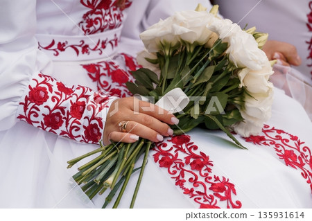 Traditional Ukrainian Wedding Dress with Red Embroidery Holding White Rose Bouquet in Cultural Celebration Traditional Ukrainian Wedding Dress with Red Embroidery Holding White Rose Bouquet in Cultural Celebration 135931614