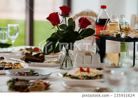 Elegant Red Rose Centerpiece on a Luxurious Banquet Table with Gourmet Dishes and Beverages in Soft Natural Light 135931624