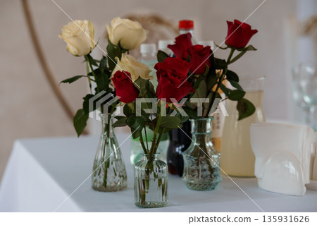 Elegant Red and White Rose Bouquet in Glass Vases on a Table with Beverage Bottles and Napkins Elegant Red and White Rose Bouquet in Glass Vases on a Table with Beverage Bottles and Napkins 135931626