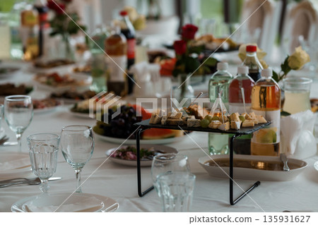 Elegant Buffet Table Setup with Cheese Platter, Fresh Fruits, Flowers, and Drinks for a Luxurious Wedding or Banquet Event Elegant Buffet Table Setup with Cheese Platter, Fresh Fruits, Flowers, and Drinks for a Luxurious Wedding or Banquet Event 135931627