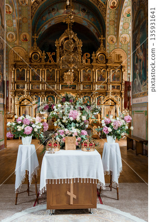 Golden Orthodox Church Interior with Ornate Iconostasis, Floral Arrangements, and Religious Artwork in Rich Blue and Gold Hues 135931641
