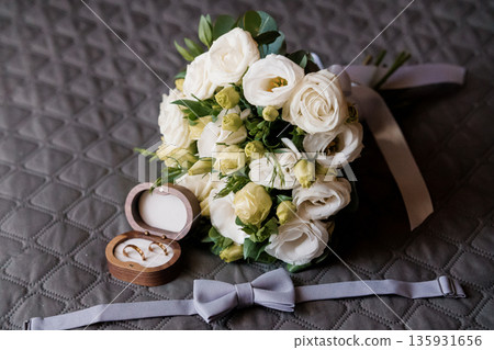 Elegant White Wedding Bouquet with Gold Rings in Wooden Box and Gray Bow Tie on Quilted Background Elegant White Wedding Bouquet with Gold Rings in Wooden Box and Gray Bow Tie on Quilted Background 135931656