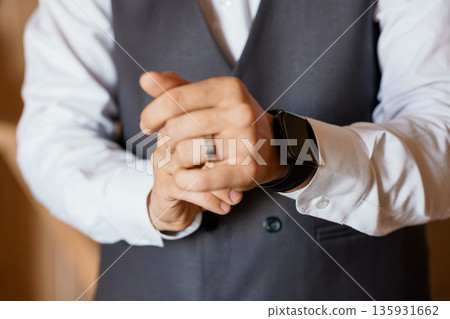 Elegant Groom Adjusting Wedding Ring and Smartwatch in Formal Gray Vest and White Dress Shirt Elegant Groom Adjusting Wedding Ring and Smartwatch in Formal Gray Vest and White Dress Shirt 135931662