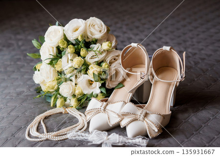 Elegant White Bridal Bouquet with Pearl-Embellished Wedding Shoes and Accessories on Quilted Gray Background Elegant White Bridal Bouquet with Pearl-Embellished Wedding Shoes and Accessories on Quilted Gray Background 135931667