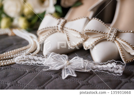 Elegant White Wedding Shoes with Pearl-Adorned Bow and Lace Garter on Quilted Fabric Background Elegant White Wedding Shoes with Pearl-Adorned Bow and Lace Garter on Quilted Fabric Background 135931668