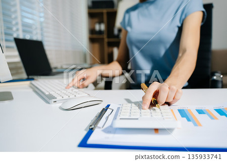 Women counting coins on calculator taking from the piggy bank. hand holding pen working on calculator to calculate on desk about cost at home office. Women counting coins on calculator taking from the piggy bank. hand holding pen working on calculator to calculate on desk about cost at home office. 135933741