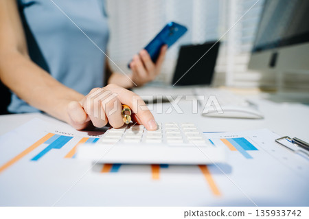 Women counting coins on calculator taking from the piggy bank. hand holding pen working on calculator to calculate on desk about cost at home office. Women counting coins on calculator taking from the piggy bank. hand holding pen working on calculator to calculate on desk about cost at home office. 135933742
