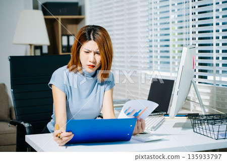 Asian woman feeling migraine head strain.Overworked businesswoman financier while working on laptop and tablet at office. 135933797
