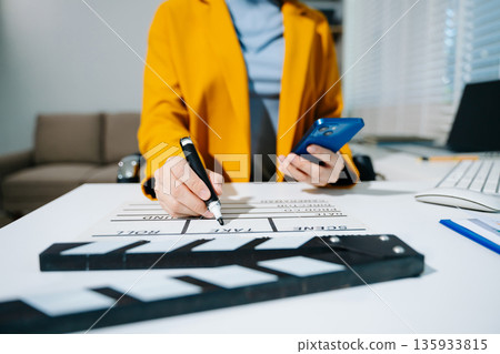 Creative female filmmaker working with tablet, clapperboard, and laptop in modern studio office. Film production, planning, and content creation scene. Creative female filmmaker working with tablet, clapperboard, and laptop in modern studio office. Film production, planning, and content creation scene. 135933815
