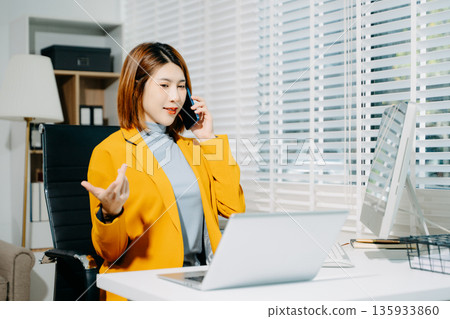 Stylish Asian woman in yellow blazer working on computer at desk in bright modern office. Confident, focused, and professional. Stylish Asian woman in yellow blazer working on computer at desk in bright modern office. Confident, focused, and professional. 135933860