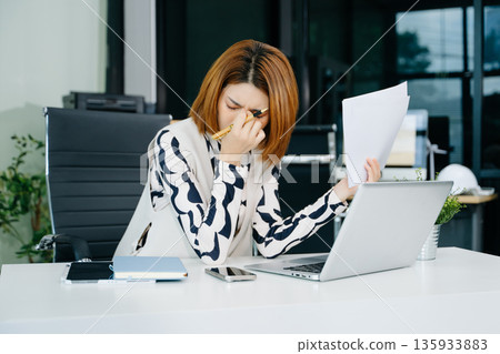 Asian business woman is stressed, bored, and overthinking from working on a tablet Asian business woman is stressed, bored, and overthinking from working on a tablet 135933883