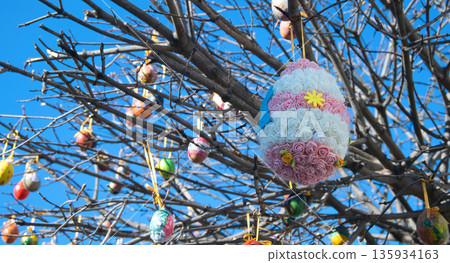 Decorated Easter eggs hanging from bare tree branches against a bright blue sky 135934163