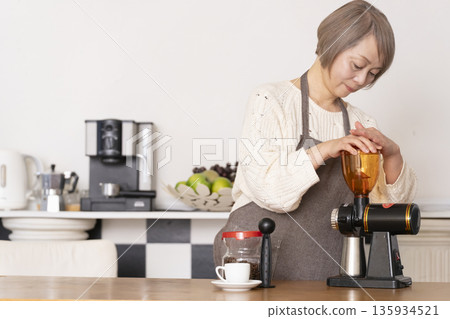 A senior woman grinding coffee beans in a coffee grinder and making espresso in an espresso machine in the kitchen 135934521