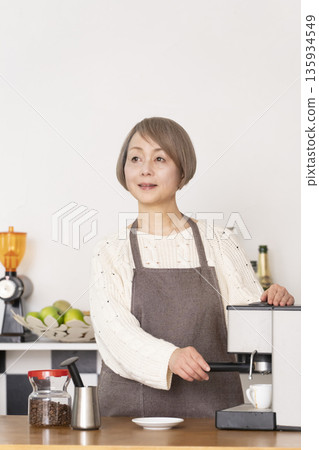 一位老婦人在廚房裡用咖啡研磨機研磨咖啡豆，並用義式咖啡機製作濃縮咖啡。 135934549