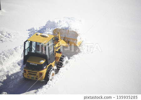 Snow removal vehicle clearing a snow-covered parking lot Snow removal vehicle clearing a snow-covered parking lot 135935285
