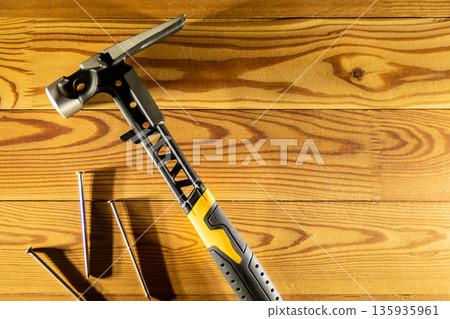 A high quality premium claw hammer accompanied by assorted nails, placed on a rustic wooden table surface, copy space, top view A high quality premium claw hammer accompanied by assorted nails, placed on a rustic wooden table surface, copy space, top view 135935961