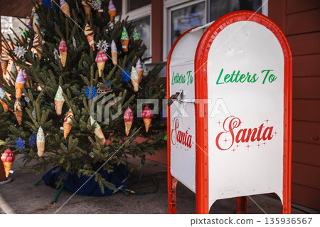 Christmas mailbox for letters to Santa standing beside a decorated holiday tree with colorful ornaments in a festive outdoor setting. 135936567
