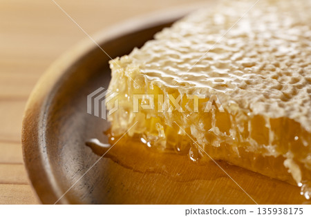 A close-up macro image of comb honey overflowing with golden honey 135938175