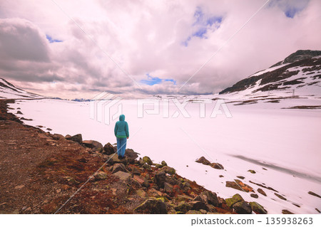 Snowy highlands during sunset. Silhouette of a young woman on the lakeshore of a frozen glacier lake at sunset. Hornsvatnet, Bjorgavegen, Aurland, Norway. Horizontal banner Snowy highlands during sunset. Silhouette of a young woman on the lakeshore of a frozen glacier lake at sunset. Hornsvatnet, Bjorgavegen, Aurland, Norway. Horizontal banner 135938263
