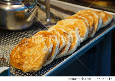 Freshly fried golden brown Korean sweet pancakes (Hotteok) displayed on a metal rack at a traditional market stall 135938416