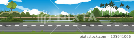 Horizontal of a scenic asphalt road passing through a lush green countryside. Landscape features a variety of trees tropical palms and dense bushes under blue sky with soft white clouds. Horizontal of a scenic asphalt road passing through a lush green countryside. Landscape features a variety of trees tropical palms and dense bushes under blue sky with soft white clouds. 135941066