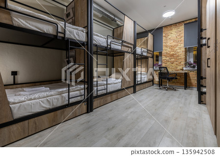 Modern hostel dormitory with wooden bunk beds, lockers and workspace at night 135942508