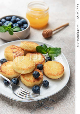 Syrniki pancakes with blueberries, fresh mint, and honey for breakfast 135942563