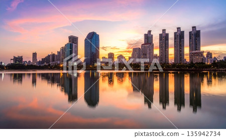 Urban cityscape panorama featuring a vibrant sunset and sunrise reflection over the river and lake water with a downtown building skyline and skyscraper view 135942734