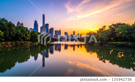 Urban cityscape panorama featuring a vibrant sunset and sunrise reflection over the river and lake water with a downtown building skyline and skyscraper view Urban cityscape panorama featuring a vibrant sunset and sunrise reflection over the river and lake water with a downtown building skyline and skyscraper view 135942736