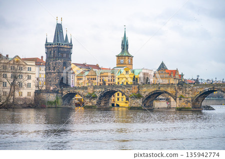 Visitors explore the historic bridge tower at Charles Bridge while enjoying views of the river and surrounding buildings in Prague. The tower stands tall against the cloudy sky. Visitors explore the historic bridge tower at Charles Bridge while enjoying views of the river and surrounding buildings in Prague. The tower stands tall against the cloudy sky. 135942774