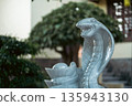 Gray stone cobra statue with open mouth in garden setting, Marble cobra sculpture guarding bonsai tree base 135943130