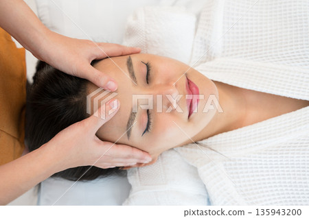 Asian smiling woman in white robe enjoying and relaxing head massage at spa salon Asian smiling woman in white robe enjoying and relaxing head massage at spa salon 135943200