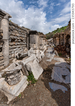 Ancient city of Ephesus ruins pathway with fallen columns and stone walls under a cloudy sky, Selcuk Turkey 135943793