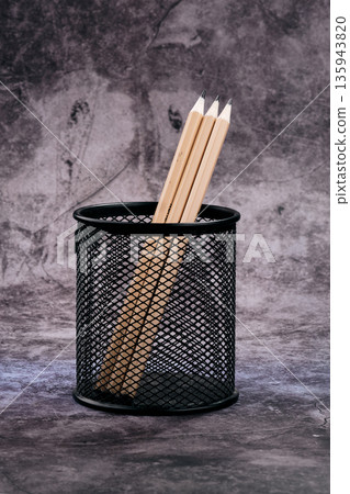 Three newly sharpened wooden pencils stand proudly in a minimalist black mesh holder Three newly sharpened wooden pencils stand proudly in a minimalist black mesh holder 135943820