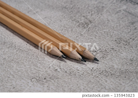 Three natural wooden pencils lie side by side on a mottled light gray background Three natural wooden pencils lie side by side on a mottled light gray background 135943823