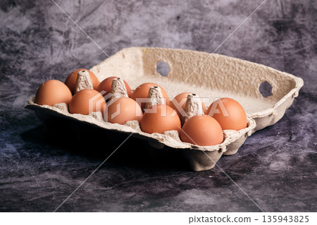 Ten warm brown eggs in an open eco-pulp carton reflect light on a dark surface, hinting at culinary use Ten warm brown eggs in an open eco-pulp carton reflect light on a dark surface, hinting at culinary use 135943825