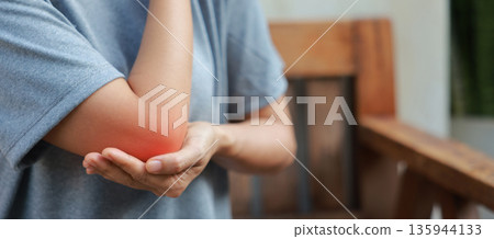 Close-up of woman hand holding painful injured elbow with red inflamed spot. Concept of joint bone pain, muscle injury, arthritis, tendonitis, or ache from sports or work in outdoor background. Close-up of woman hand holding painful injured elbow with red inflamed spot. Concept of joint bone pain, muscle injury, arthritis, tendonitis, or ache from sports or work in outdoor background. 135944133